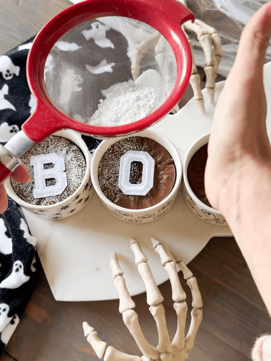 Easy halloween brownies with BOO design on ghost tray. Sprinkling on powdered sugar. Skeleton hands with ghost towel for added decor.