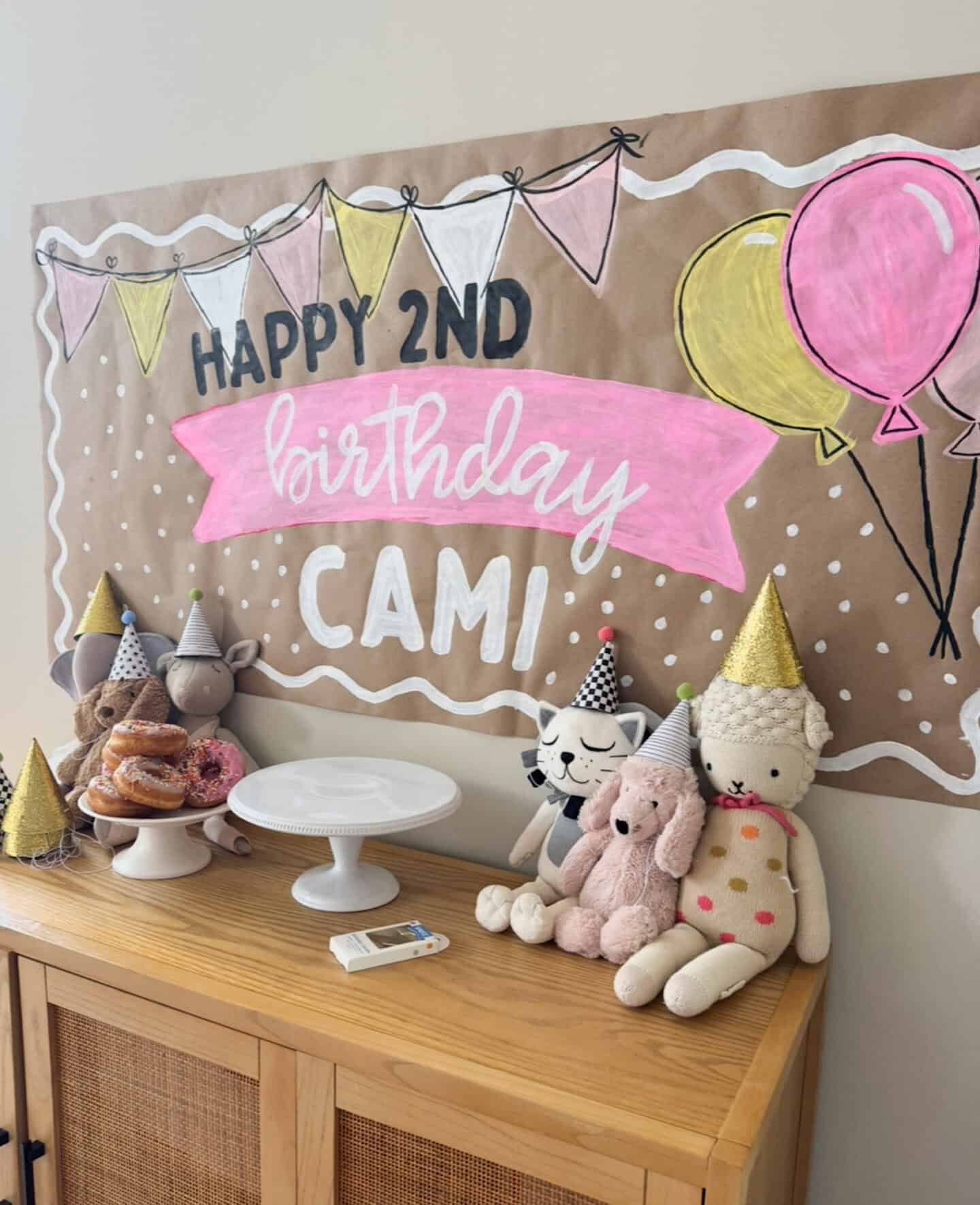 painted birthday banner with stuffed animals on table and sprinkle donuts