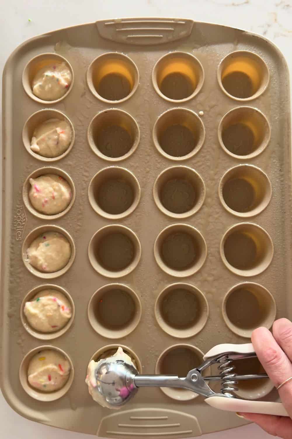Scooping sprinkle muffin batter into a silicone mini muffin tray
