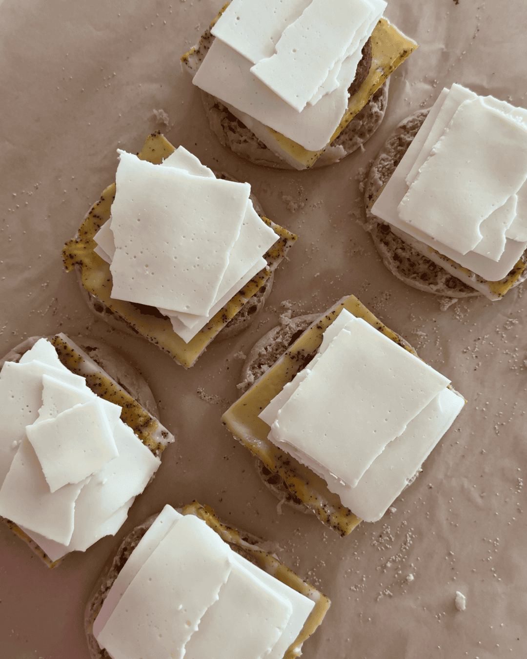 Assembling freezer breakfast sandwiches with egg, sausage patty, and sliced cheese on English muffins